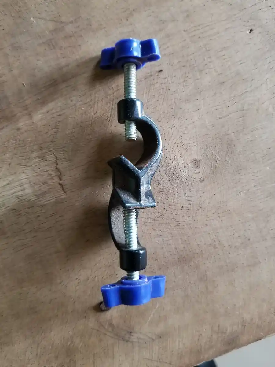 A right-angle boss head with two blue thumbscrews, laid on a wooden bench