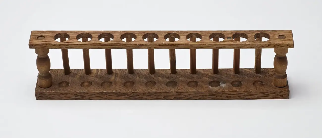 A wooden test-tube rack with turned end posts, holes along the top rail and drying pegs below