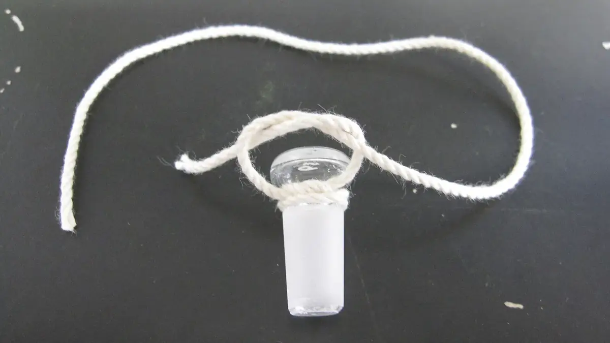 A ground-glass stopper lying on a dark bench with its cotton tie